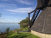 Backside of historic windmill Doris Mooltsje, Oudega, Sudwest-Fryslan, Friesland, Netherlands  Backside of historic windmill Doris Mooltsje, Oudega, Sudwest-Fryslan, Friesland, Netherlands : windmill, Doris Mooltsje, Oudega, Aldegea, Sudwest-Fryslan, Friesland, Netherlands, Dutch, europe, european, building, architecture, monument, historic, history, culture, dutch culture, travel destination, destination, black, 4, four, rural, landscape, rural landscape, outside, outdoor, outdoors, no people, nobody, season, summer, summertime, sky, blue sky, white clouds, grass, lake, water
